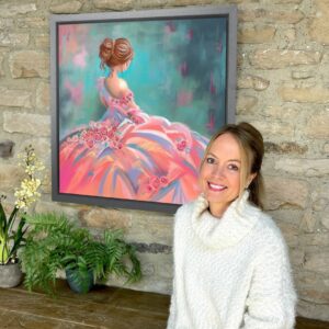 image of Lucy Pittaway, artist, sat in front of one of her paintings from the Ladies collection, currently on display at The Station in Richmond, North Yorkshire.