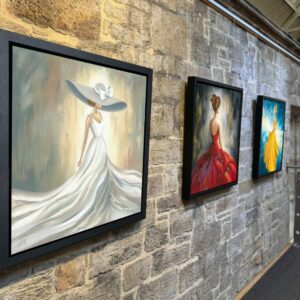 Framed prints from the Ladies Collection hanging on an exposed stone wall at The Station in Richmond, North Yorkshire, featuring elegant women in flowing dresses in soft pastel, bold red and bright yellow tones