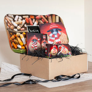 Gift box with a teddy bear in a red hat and scarf, surrounded by various items on a light background.